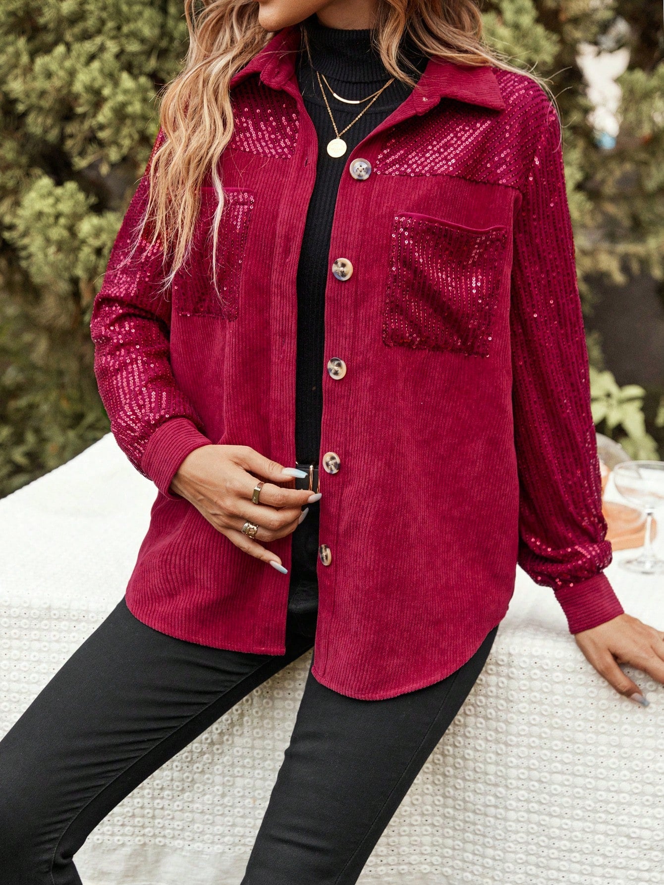 model sitting on a white table, wearing a Red glitter jacket with a black outfit