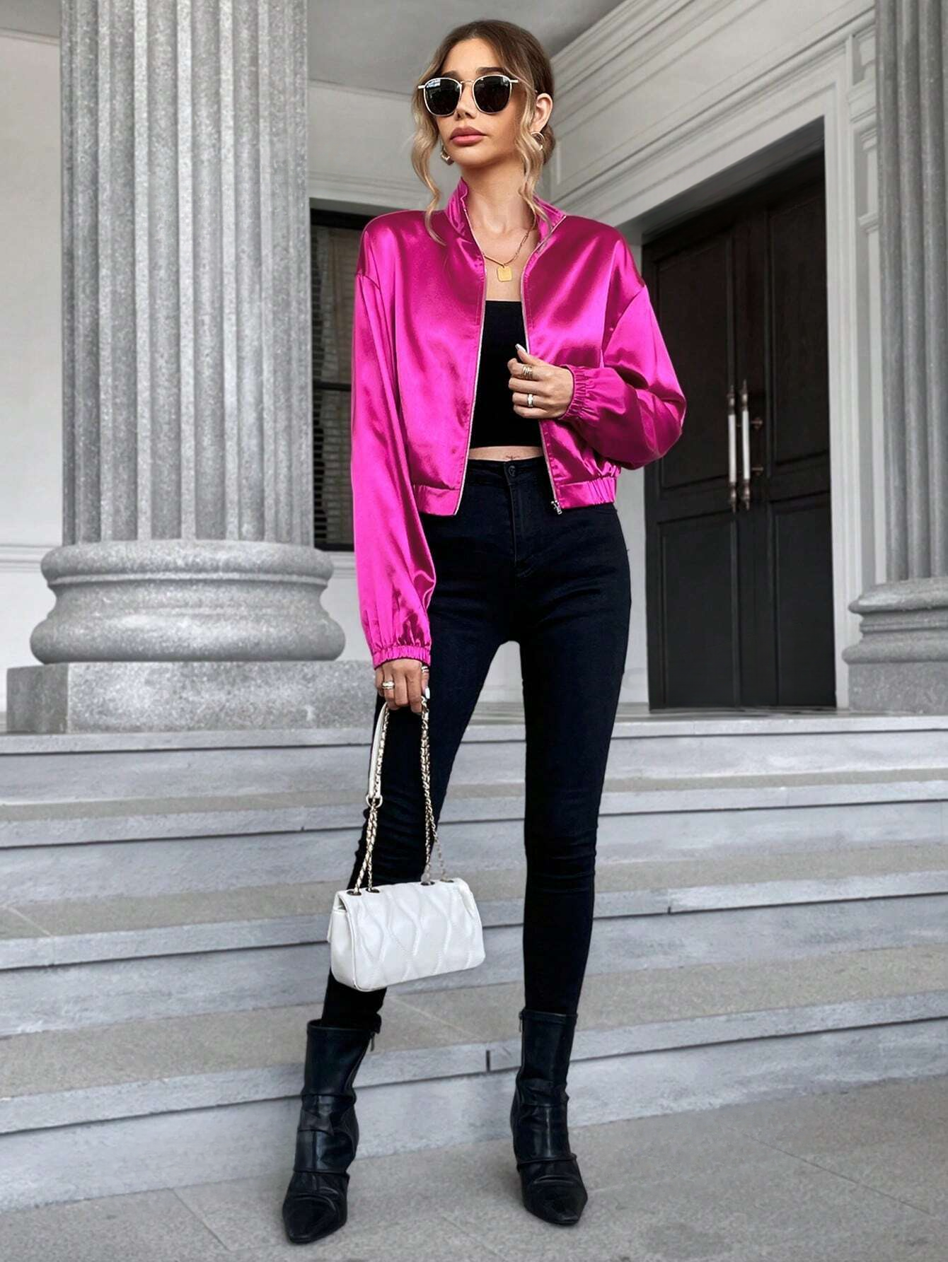 full body picture of a model wearing a Hot pink metallic jacket with a black slim pants and a white bag